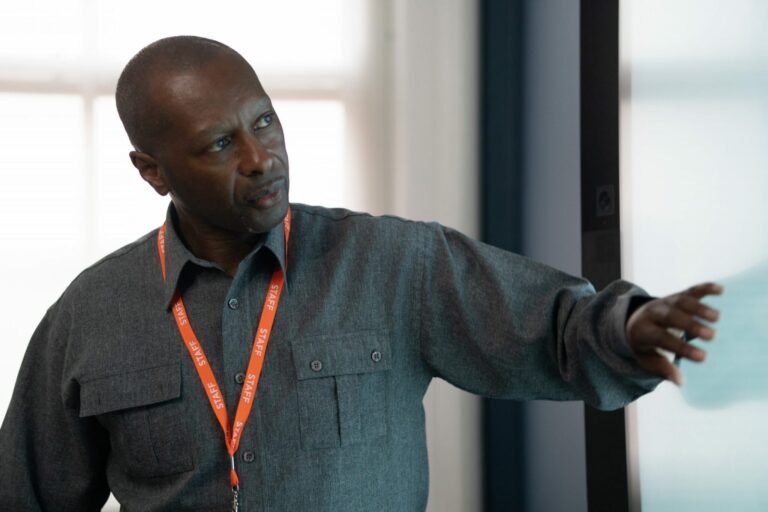 Man wearing a staff lanyard pointing at an interactive display screen during a presentation or training session.